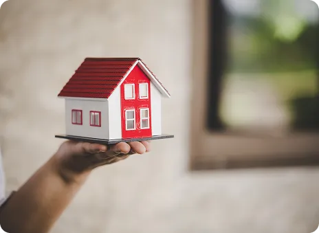 Hand holding a small white and red model house with blurred background.