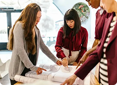 Four diverse professionals reviewing architectural blueprints in a well-lit office.