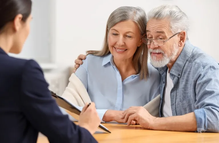 Elderly couple attentively reviewing documents with a professional woman at a wooden table.