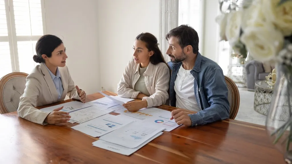 Three adults, two women and one man, engaged in a discussion over financial documents at a wooden table.