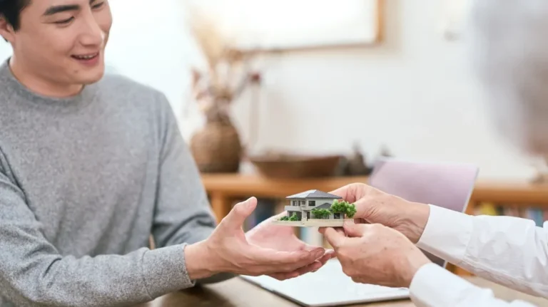 Two people exchanging a miniature model of a modern house indoors.