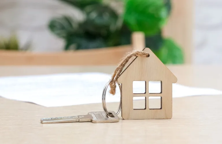 Wooden house-shaped keychain with a metal key on a light wooden surface.